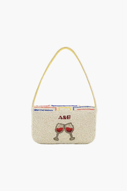 Beige handbag with red wine glass design and initials on a white background