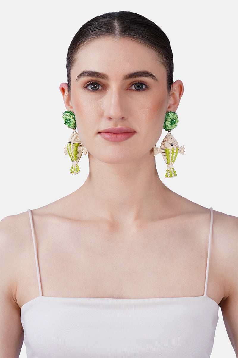 Woman wearing green and gold earrings against a white background